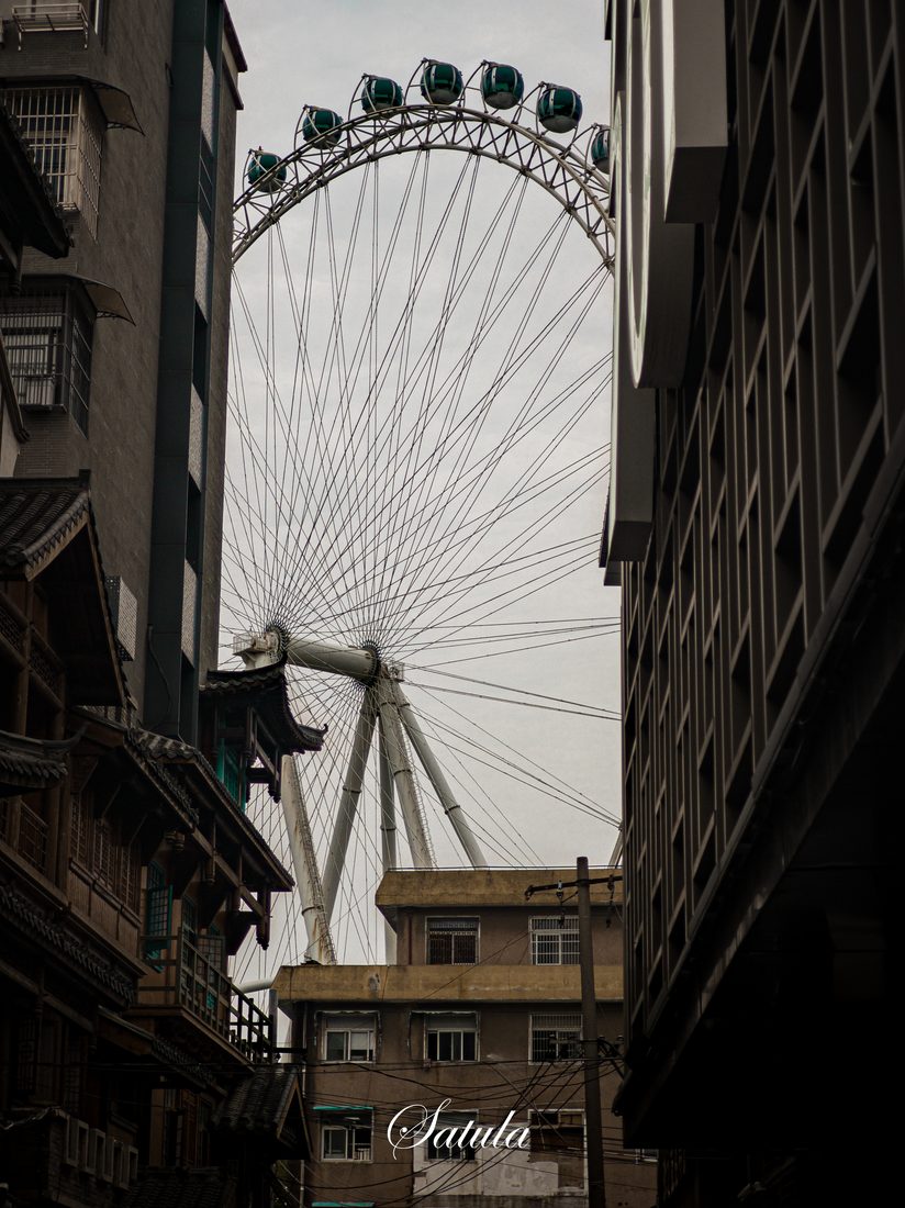 摩天轮夹在两侧城市建筑之间，向天空升起。